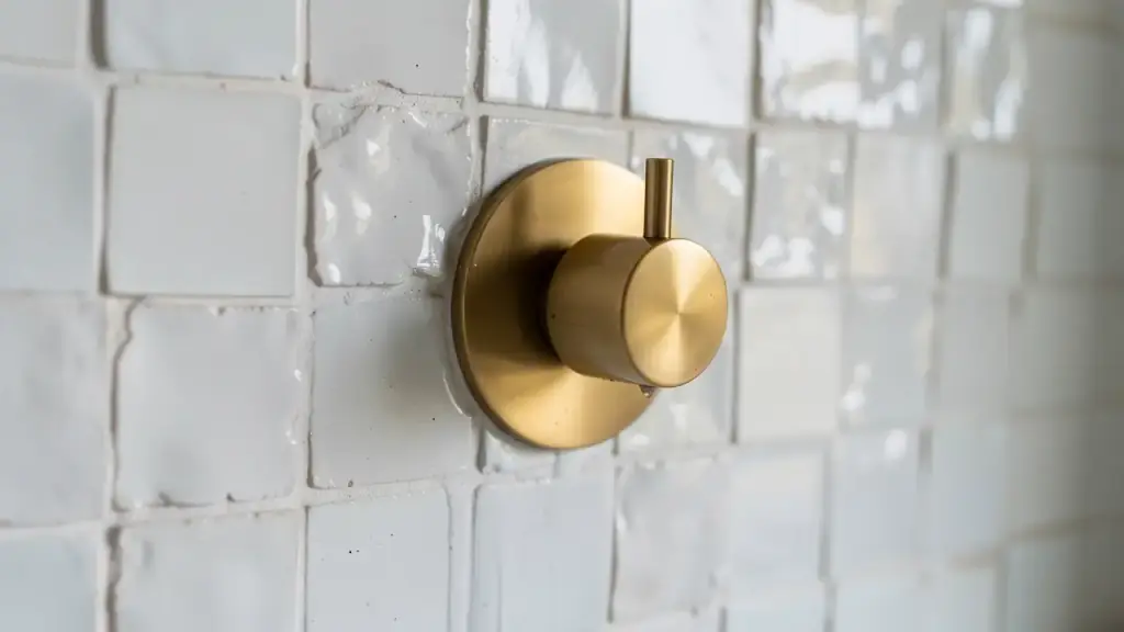 Glossy white zellige tile around a brushed brass shower valve