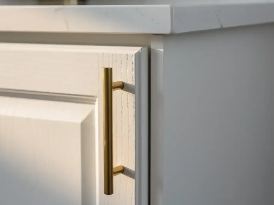 A painted shaker cabinet door with a brass pull beside a quartz counter edge and a clean caulk line