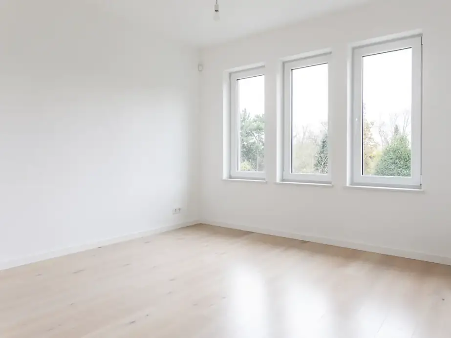 A new room with white walls, an oak floor and three tall windows